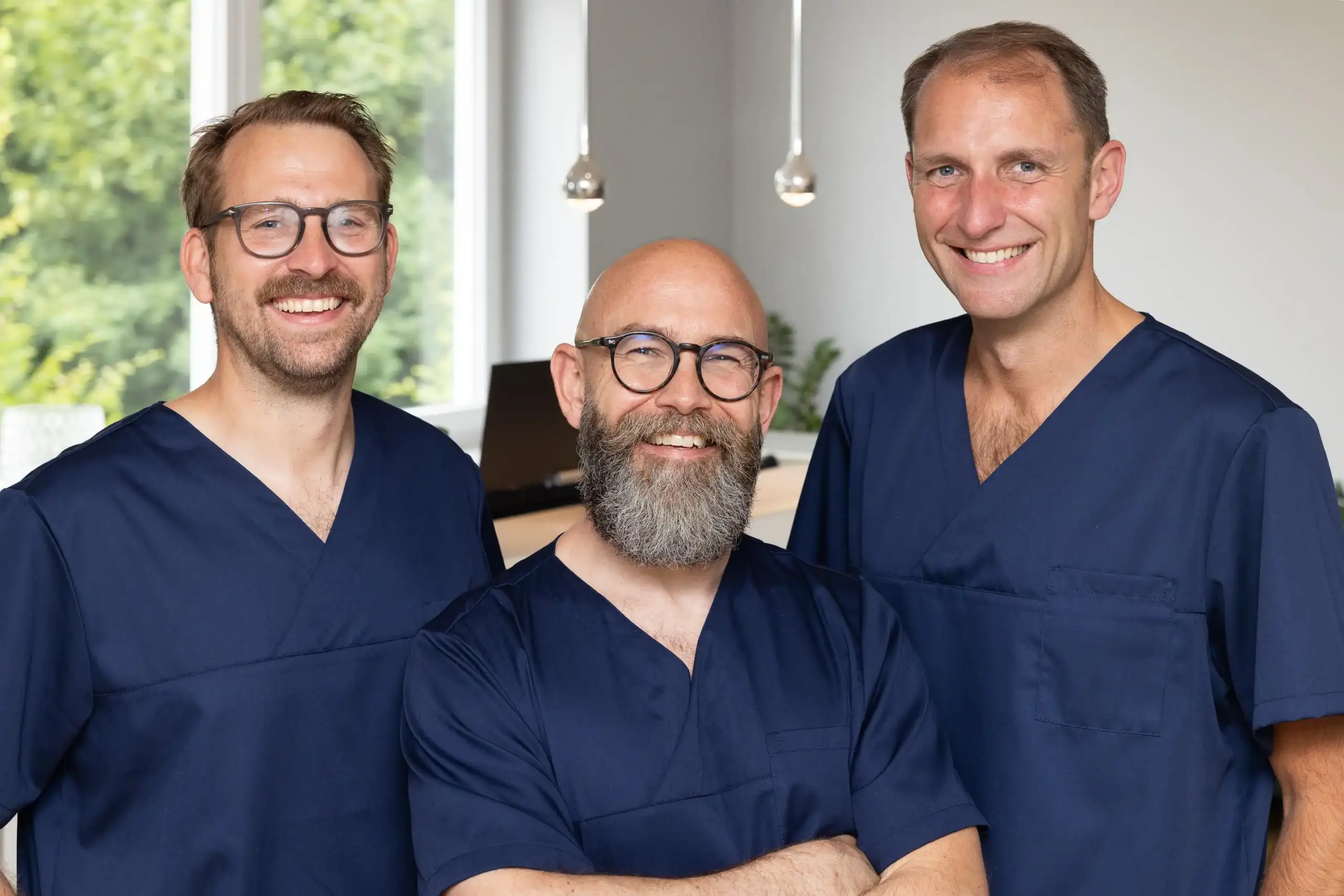Drei Anästhesisten in blauer OP-Kleidung stehen nebeneinander und lächeln in die Kamera.