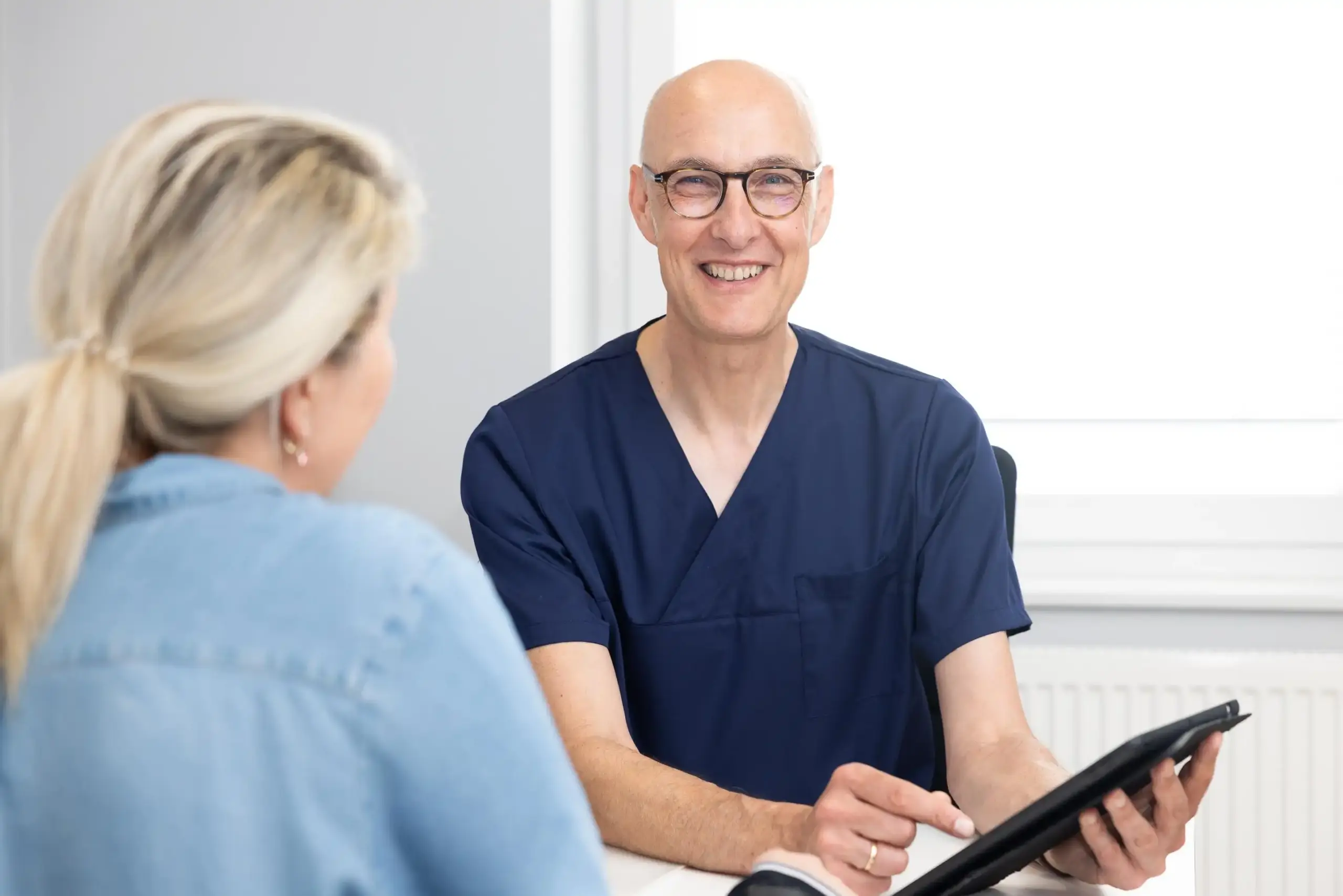 Anästhesist sitzt im Beratungsraum und führt ein Gespräch mit einer Patientin, die ihm gegenübersitzt.